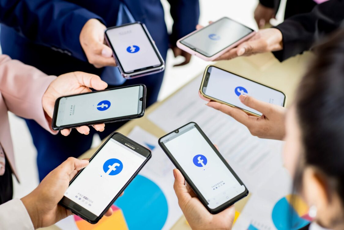 Facebook for Nonprofit Websites: Six hands holding mobile phones that are on Facebook.